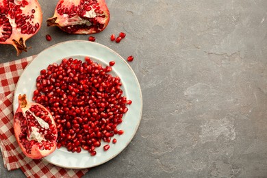 Photo of Tasty ripe pomegranate and grains on grey table, flat lay. Space for text
