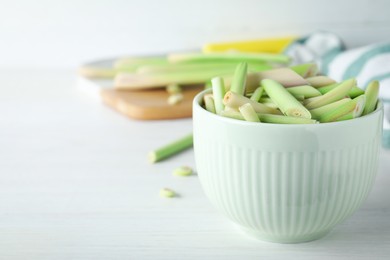 Photo of Bowl with fresh lemongrass stalks on white table, closeup. Space for text