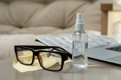 Photo of Glasses, microfiber cloth and spray bottle on table indoors