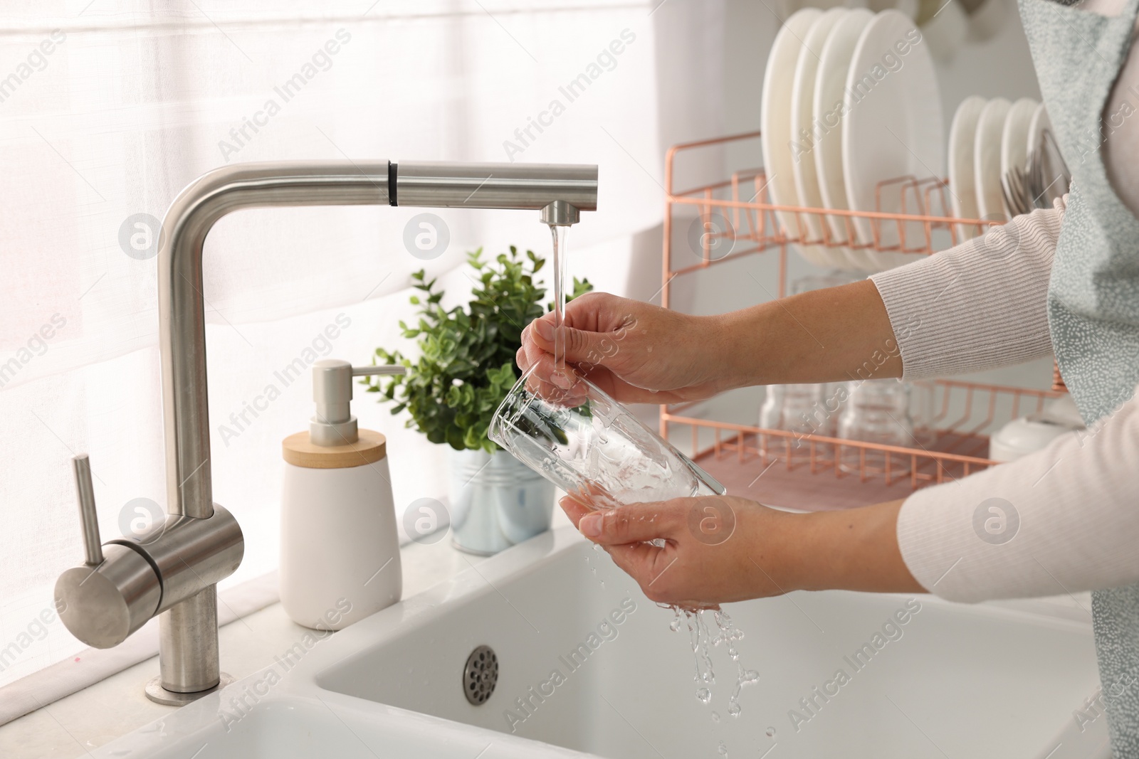 Photo of Woman washing glass at sink in kitchen, closeup