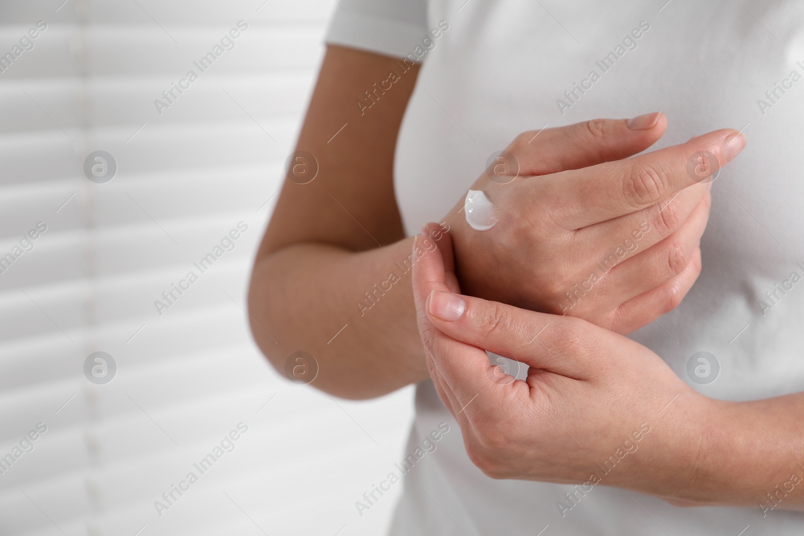 Photo of Woman applying cosmetic cream onto hand on blurred background, closeup. Space for text