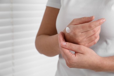 Woman applying cosmetic cream onto hand on blurred background, closeup. Space for text