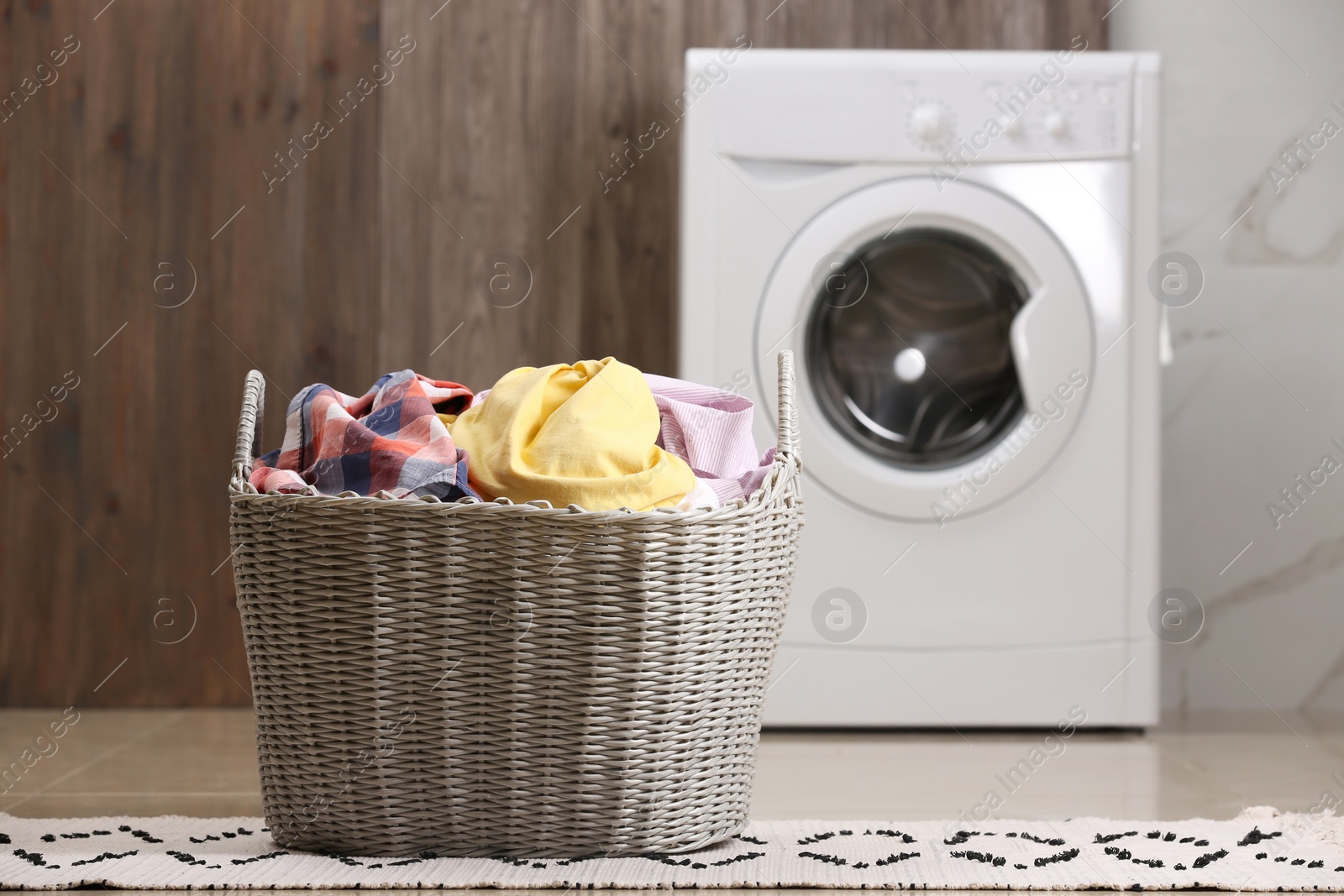 Photo of Wicker basket with dirty clothes on floor in laundry room