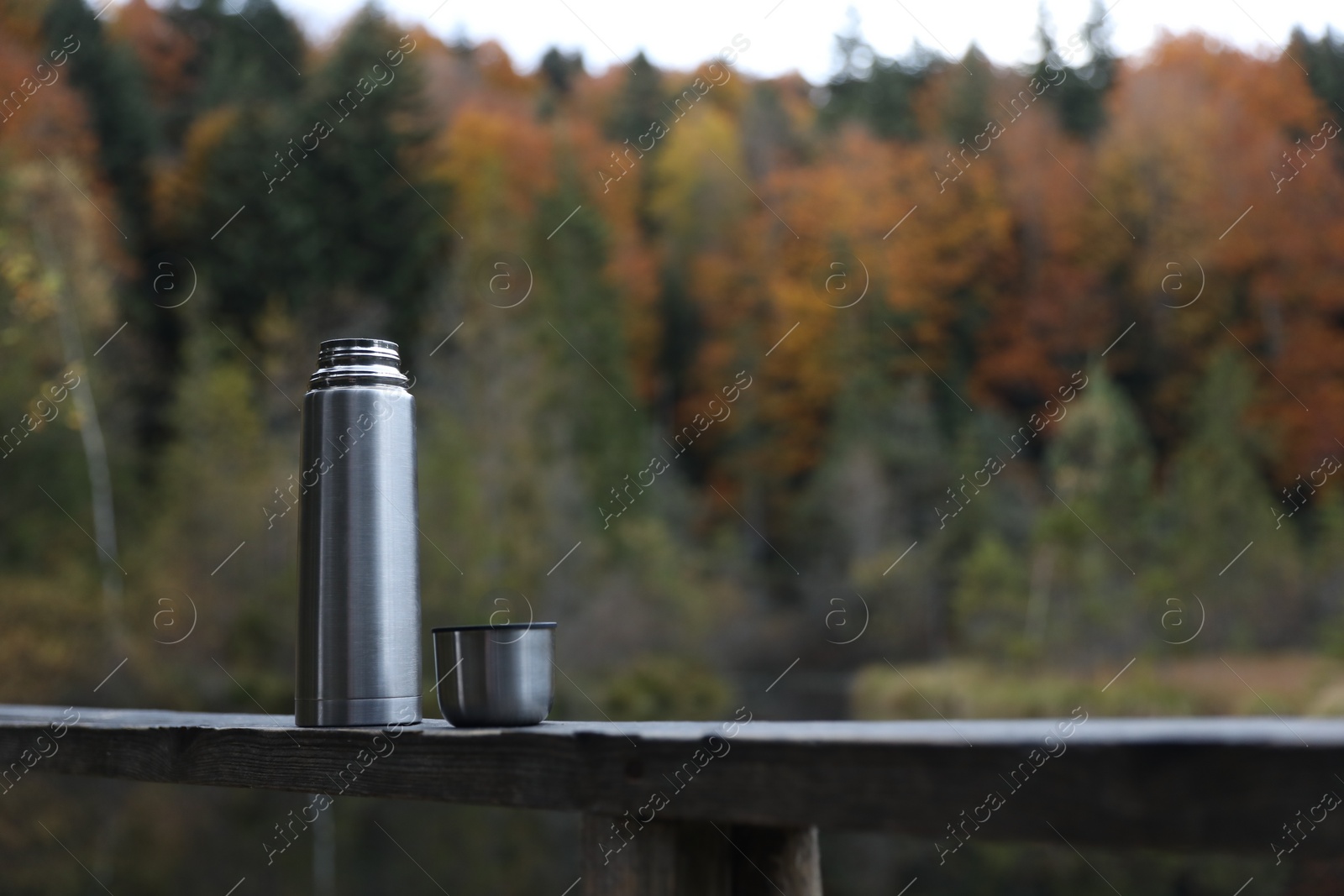 Photo of Metallic thermos and cup lid on handrail outdoors, space for text