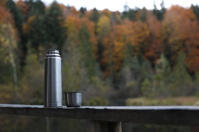 Photo of Metallic thermos and cup lid on handrail outdoors, space for text