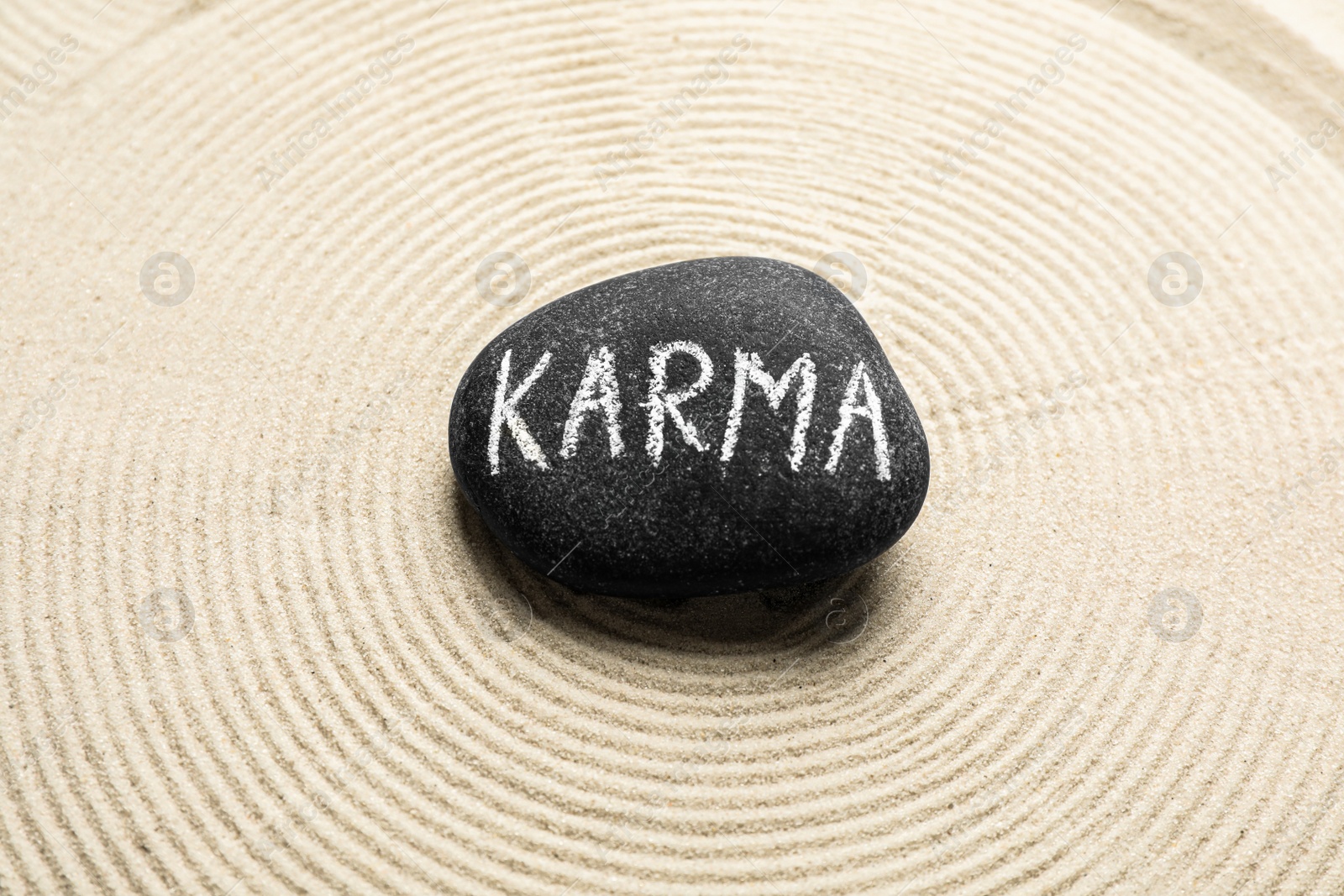 Photo of Stone with word Karma and circles on sand, top view