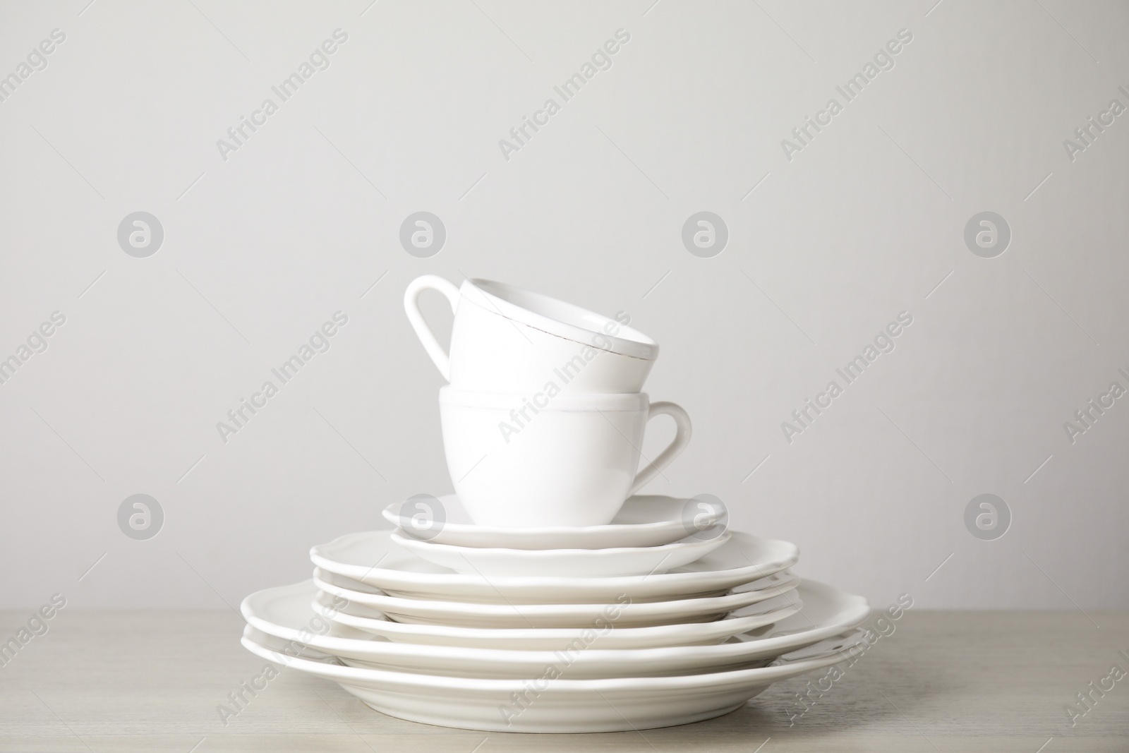 Photo of Stack of clean plates and cups on table against white background