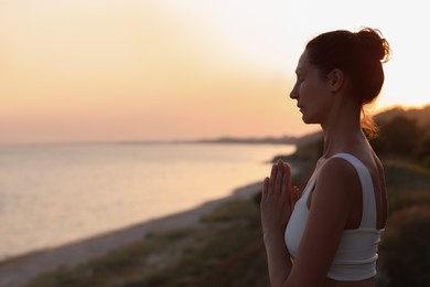 Photo of Mature woman meditating near sea in evening. Space for text