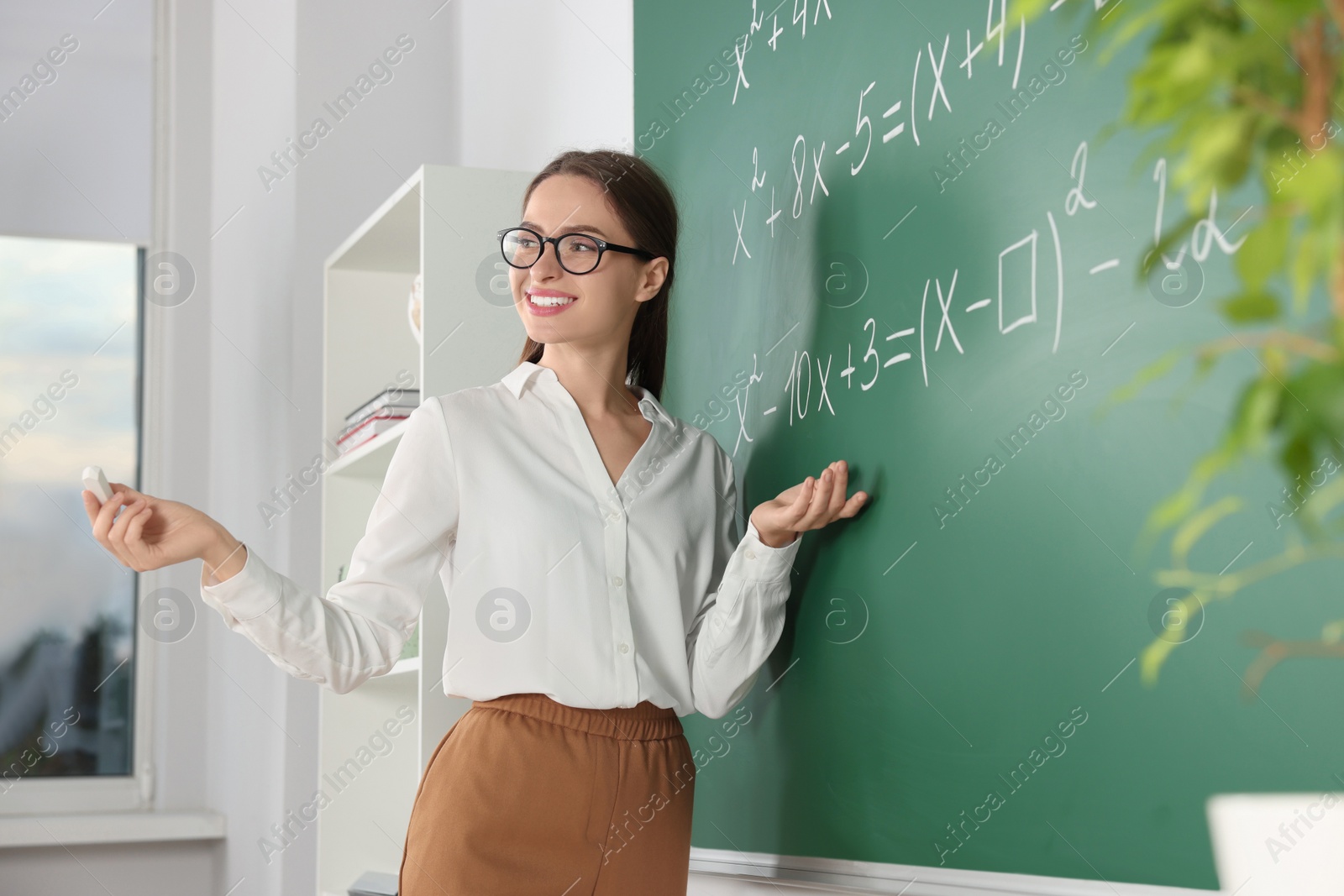 Photo of Young math’s teacher explaining mathematical equations near chalkboard in classroom