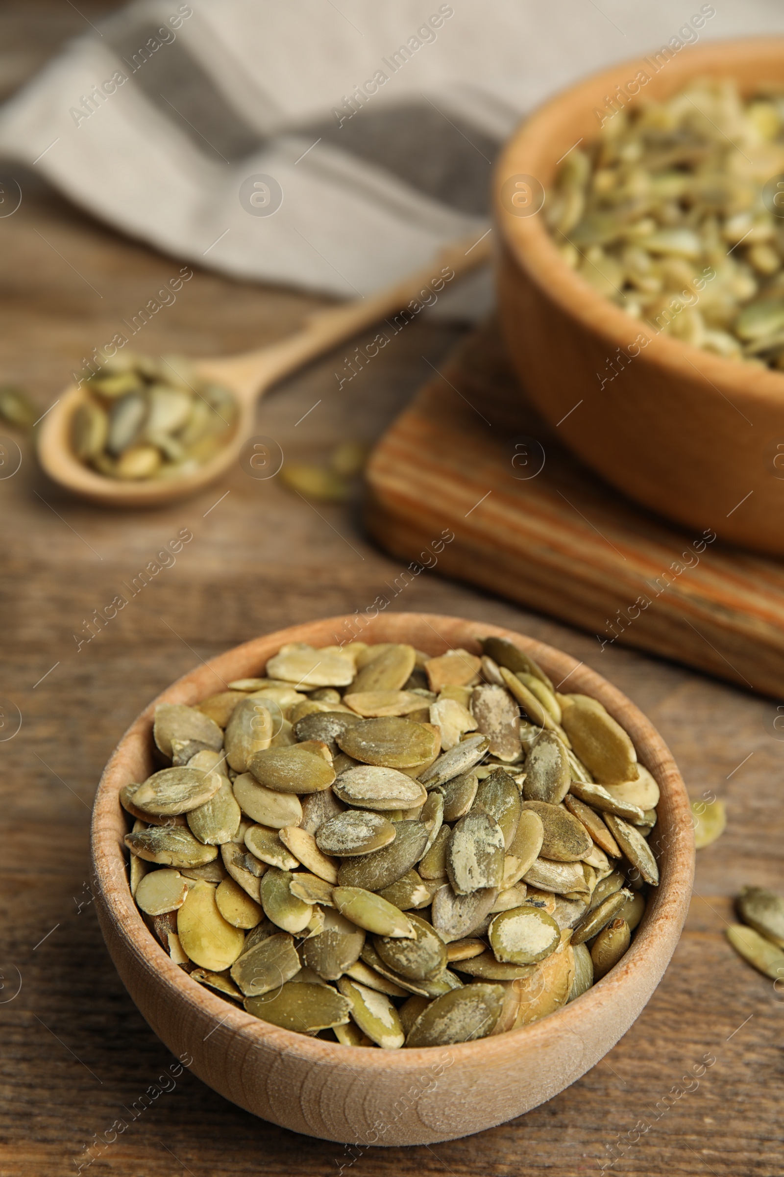 Photo of Bowl of raw peeled pumpkin seeds on wooden table. Space for text