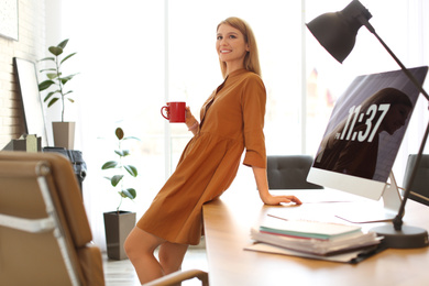 Young woman with cup of drink relaxing in office during break