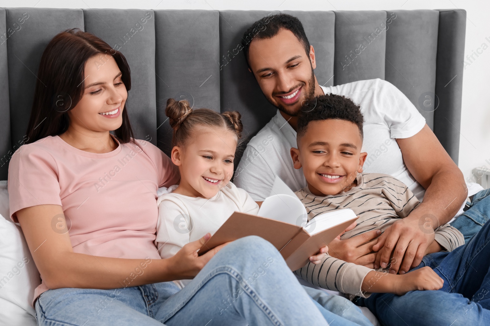 Photo of Happy international family reading book on bed