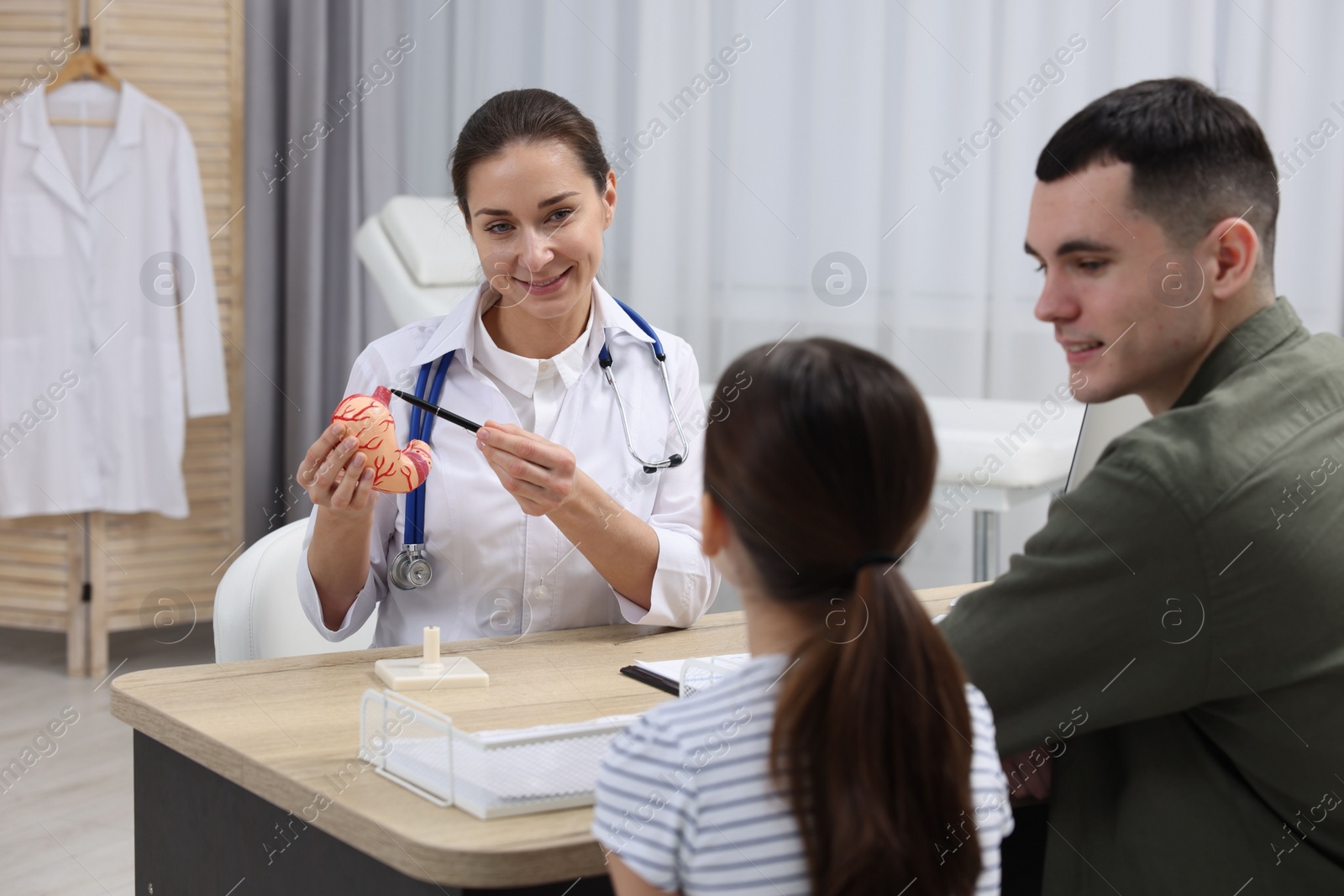 Photo of Gastroenterologist with model of stomach consulting man and his daughter in clinic