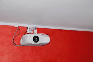 Photo of Modern digital video projector on red wall indoors. Space for text