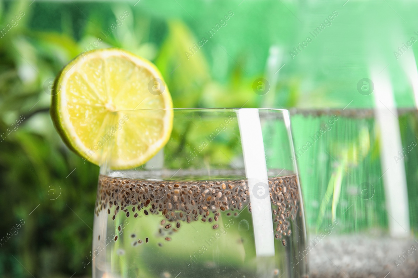 Photo of Glass of water with chia seeds and lime slice on blurred background, closeup