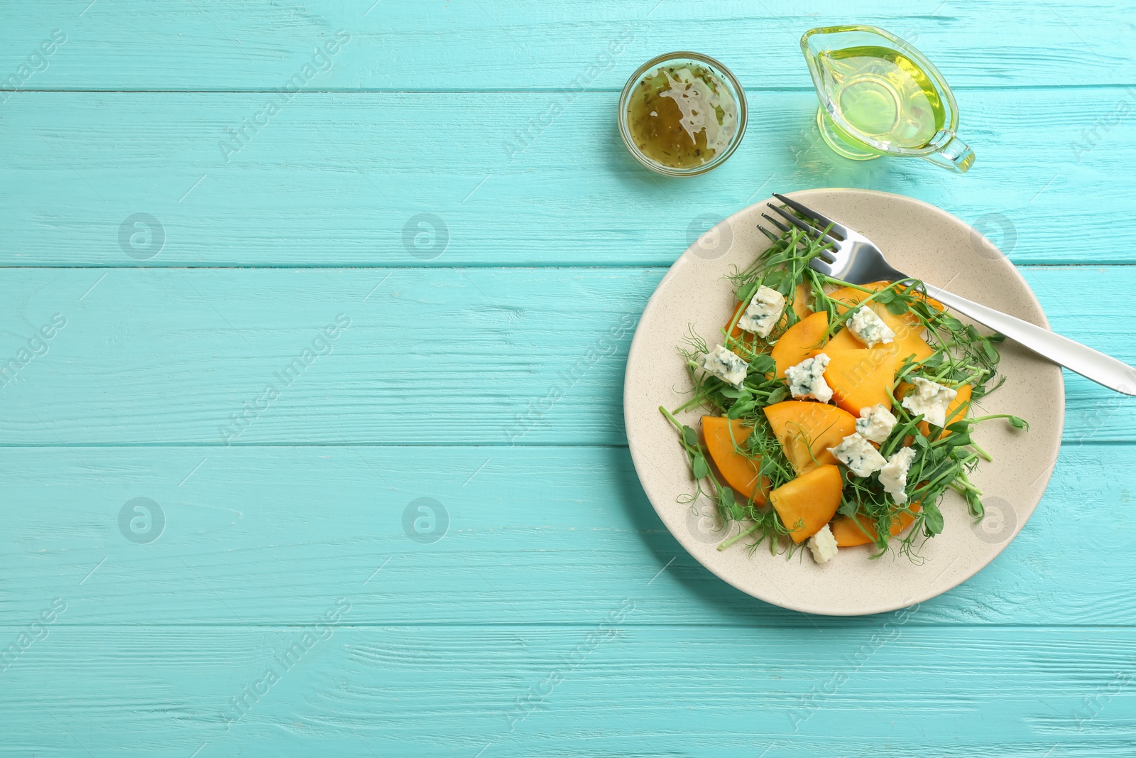 Photo of Delicious persimmon salad with blue cheese on light blue wooden table, flat lay. Space for text