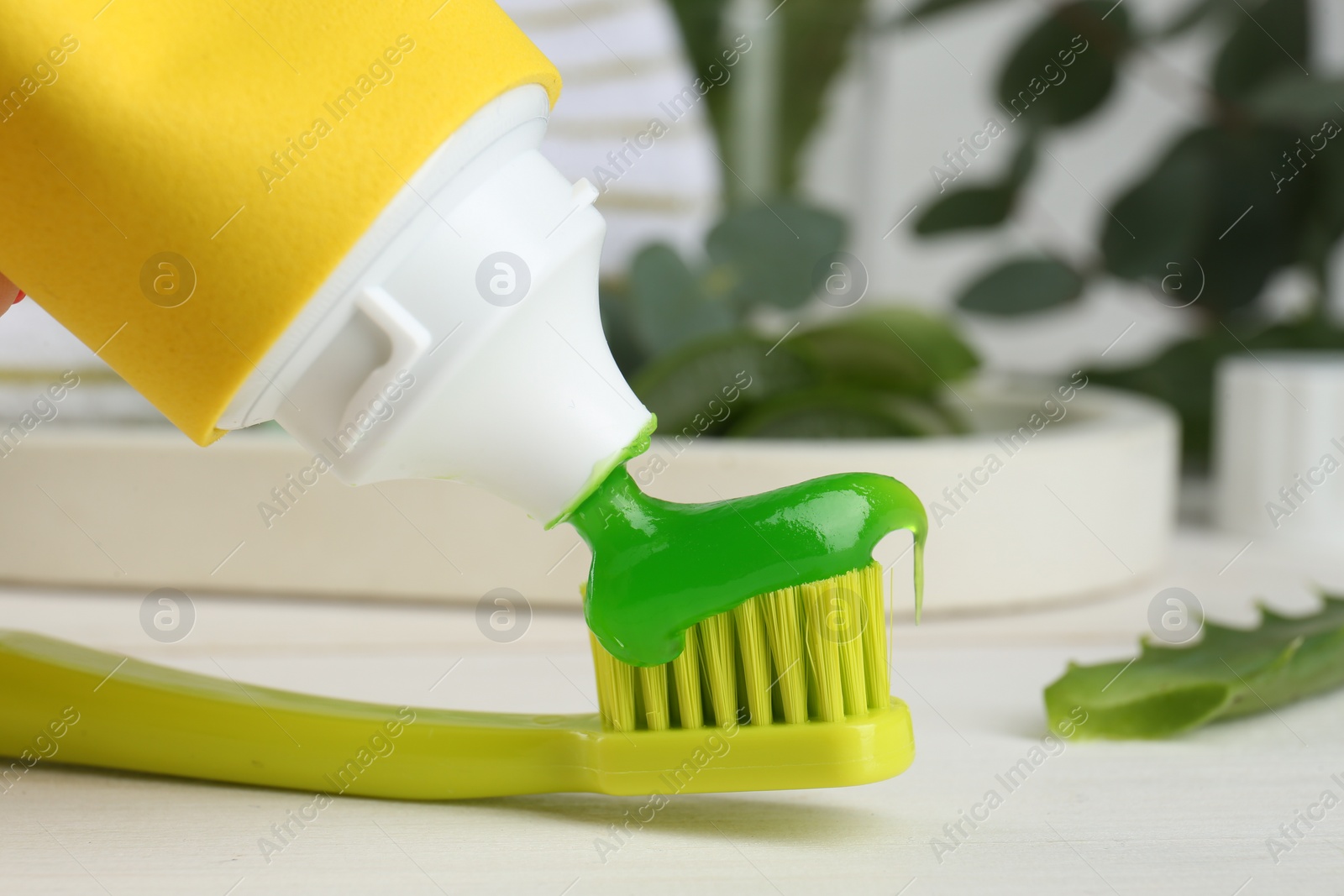 Photo of Applying aloe toothpaste on toothbrush at white table, closeup