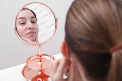 Photo of Woman with acne problem looking at mirror indoors