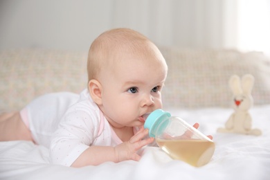 Pretty baby drinking from bottle on bed at home