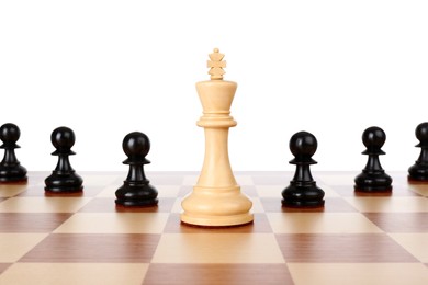 Photo of King among black pawns on wooden chess board against white background