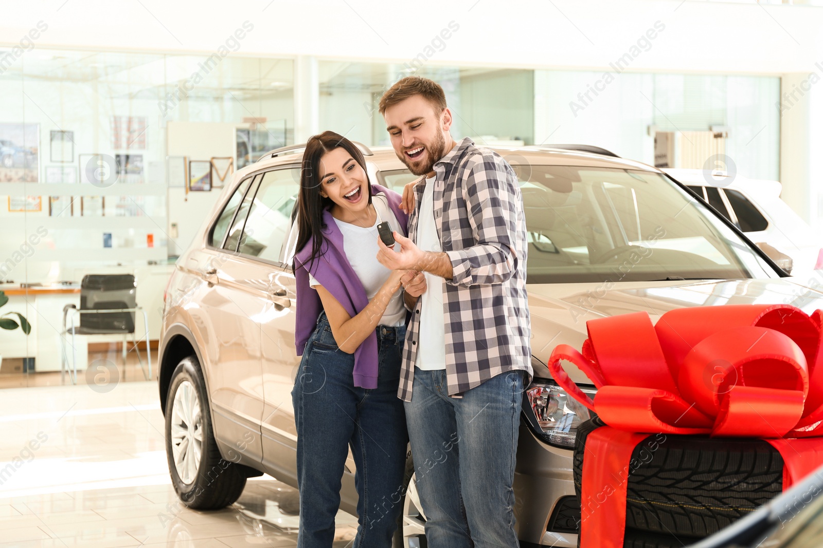 Photo of Happy couple with car key in modern auto dealership