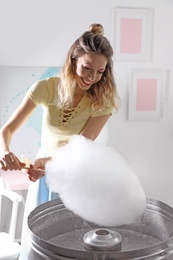 Photo of Young woman making cotton candy using modern machine in room