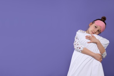 Girl with sleep mask and pillow on purple background, space for text. Insomnia problem