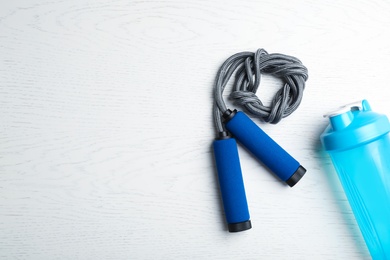 Photo of Jump rope, bottle of water and space for text on white wooden background, top view