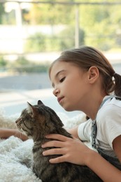 Photo of Cute little girl with her cat near window at home. Childhood pet