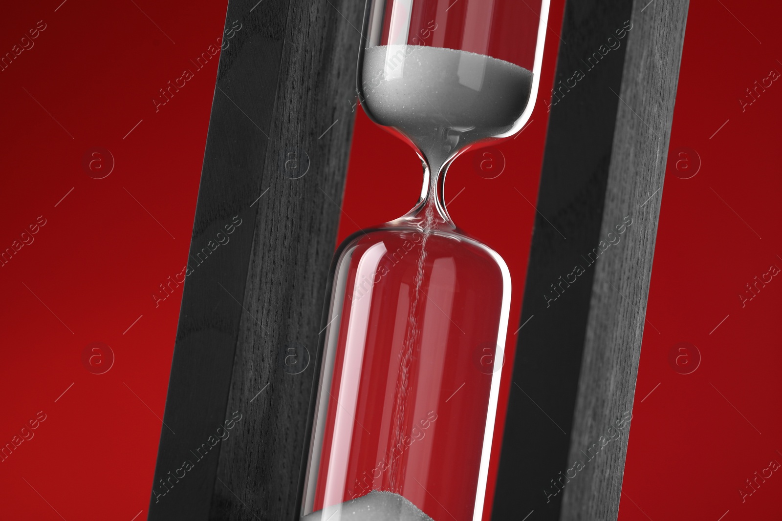 Photo of Hourglass with flowing sand on red background, closeup