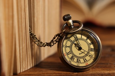 Photo of Pocket clock with chain and book on wooden table, closeup