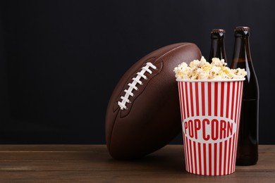 Photo of American football ball with popcorn and beer on wooden table. Space for text