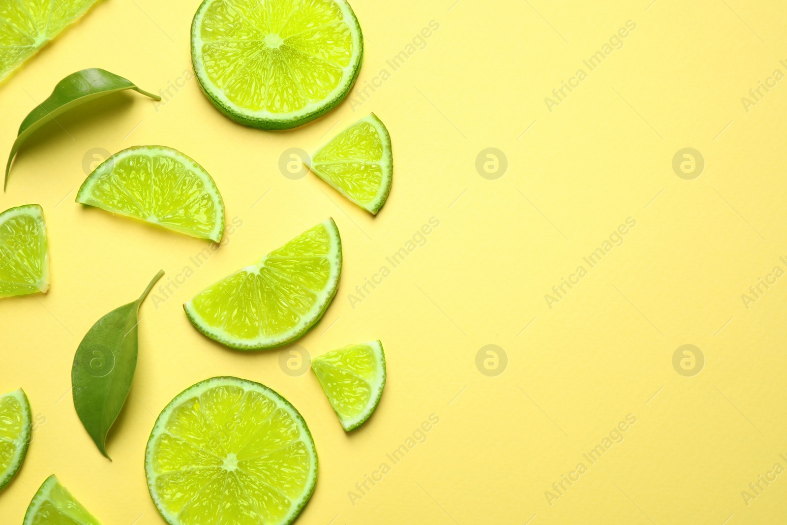 Photo of Juicy fresh lime slices and green leaves on yellow background, flat lay. Space for text