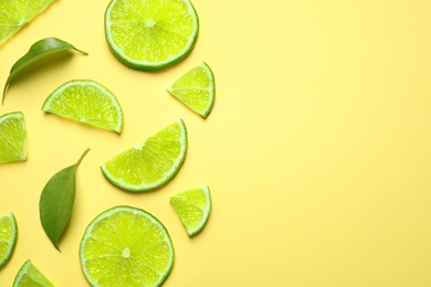 Photo of Juicy fresh lime slices and green leaves on yellow background, flat lay. Space for text