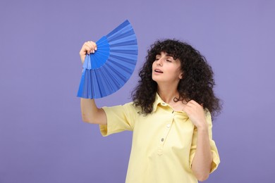 Photo of Woman with hand fan suffering from heat on purple background