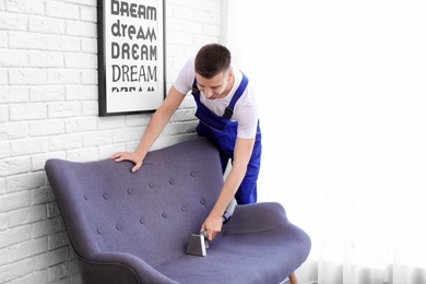 Dry cleaning worker removing dirt from sofa indoors