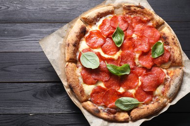 Photo of Tasty pepperoni pizza with basil on black wooden table, top view. Space for text