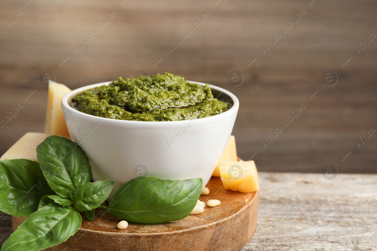 Photo of Tasty pesto sauce in bowl, basil, cheese and pine nuts on wooden table, space for text
