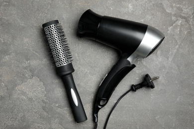 Photo of Hair dryer and brush on grey marble table, flat lay. Professional hairdresser tool