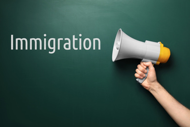 Man holding megaphone near chalkboard with word IMMIGRATION