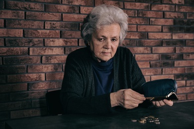 Photo of Poor mature woman pouring coins out of wallet at table