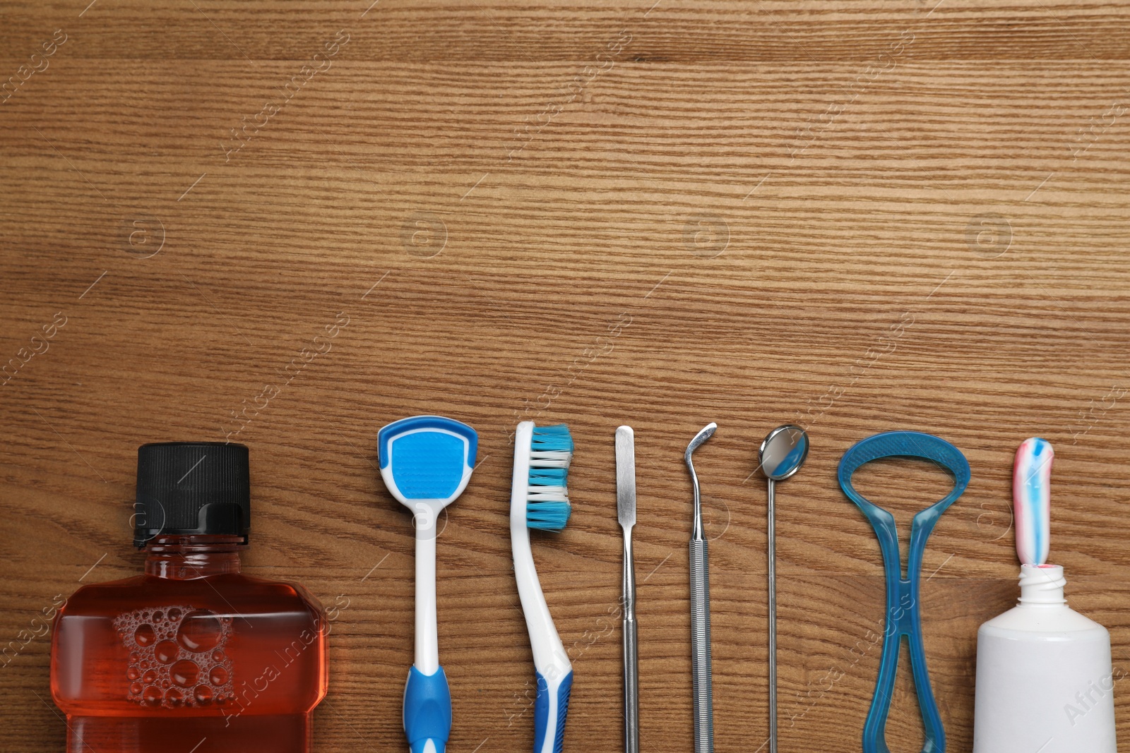 Photo of Flat lay composition with tongue cleaners, dentist instruments and teeth care products on wooden table, space for text