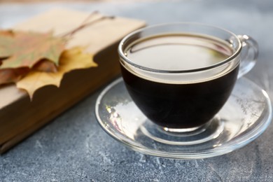 Glass cup with coffee and book on grey table, closeup. Morning ritual