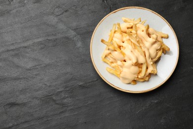 Photo of Delicious French fries with cheese sauce on black table, top view. Space for text