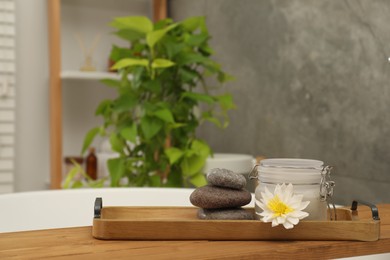 Spa products and beautiful flower on wooden tub tray in bathroom