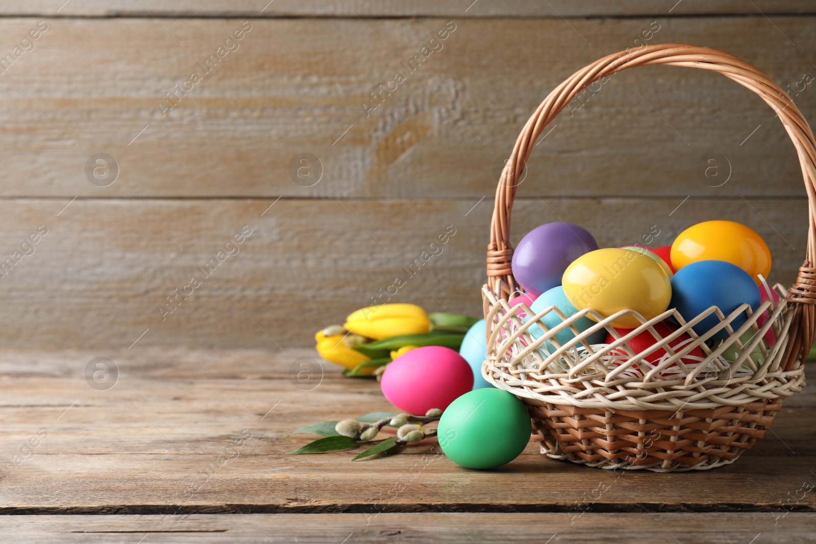 Photo of Colorful Easter eggs in wicker basket on wooden background. Space for text