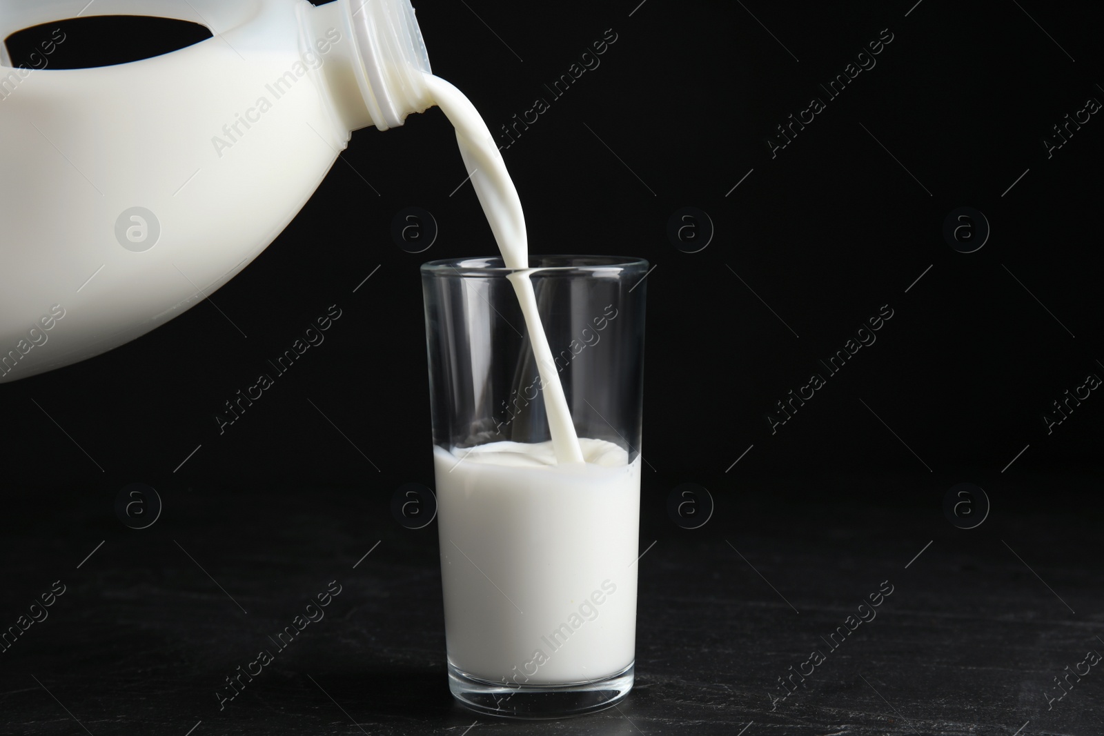 Photo of Pouring milk from gallon bottle into glass on black table