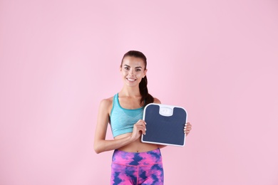 Happy young woman with scales on color background. Weight loss motivation