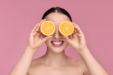 Photo of Beautiful young woman covering face with pieces of orange on pink background