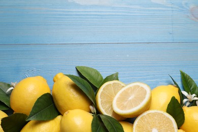 Many fresh ripe lemons with green leaves and flowers on blue wooden table, flat lay. Space for text